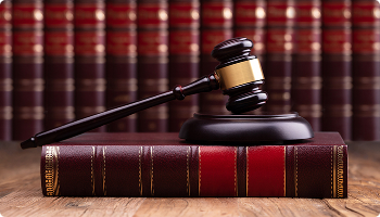 Wooden judge's gavel and sound block resting on a thick leather-bound law book with a row of legal volumes blurred in the background