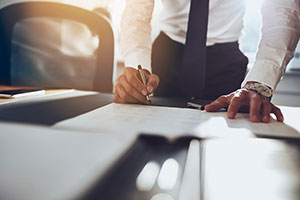 Close-up of a businessman in a white shirt and tie leaning over a desk to sign legal or corporate documents.